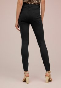 Leggings negros de cintura alta con un ajuste ceñido, que cuentan con bolsillos traseros y una textura suave. Combinados con tacones dorados de tiras.