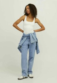Top de tirantes blanco ajustado, jeans de tiro alto azul claro y una chaqueta de mezclilla atada a la cintura, combinados con zapatillas blancas.