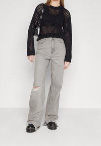 Maglione nero a maglia aperta, jeans grigi a vita alta con dettagli strappati e stivali neri con suola spessa. Una borsa minimalista completa il look.