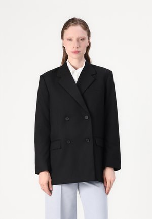 Svart dobbelspent blazer med skreddersydd passform, store revers og to frontlommer. Har glatt stoff og knappelukking.