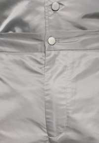 Grått tyg med satinfinish och en slät yta har silverfärgade metallknappar och en diskret sidoficka till vänster.