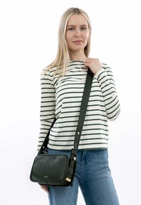 Černá kožená crossbody taška s texturovaným povrchem, obdélníkovým tvarem, zlatými akcenty a nastavitelným popruhem. Nosená s pruhovaným topem a džíny.