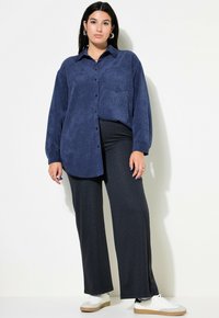 Marineblauw overhemd met knopen in een zachte stof, lange mouwen en een borstzak, gecombineerd met zwarte pantalon met pinstripes en witte sneakers.