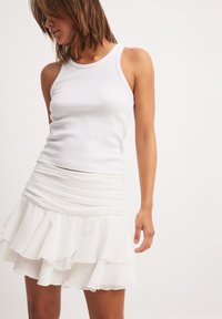 Witte geribde tanktop gecombineerd met een gelaagde witte rokken met ruches, met een aansluitende taille en zachte, vloeiende stof met een gladde textuur.