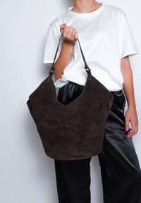 Borsa hobo in suede marrone con una base ampia e arrotondata e una parte superiore a forma di V. Presenta cinture in pelle e una superficie morbida e testurizzata.