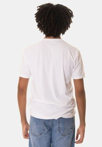 T-shirt bianco a maniche corte con scollatura rotonda, realizzato in morbido cotone. Indossato con jeans in denim blu chiaro con tasche posteriori.