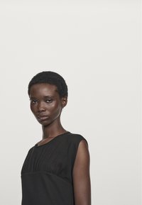 Schwarzes ärmelloses Top mit gefaltetem Vorderdesign, das einen runden Ausschnitt und einen weichen Stoff hat. Schlichte und elegante Silhouette.