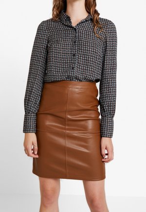 Blusa a quadri con maniche lunghe e chiusura a bottoni, abbinata a una gonna in pelle marrone aderente con cuciture verticali.