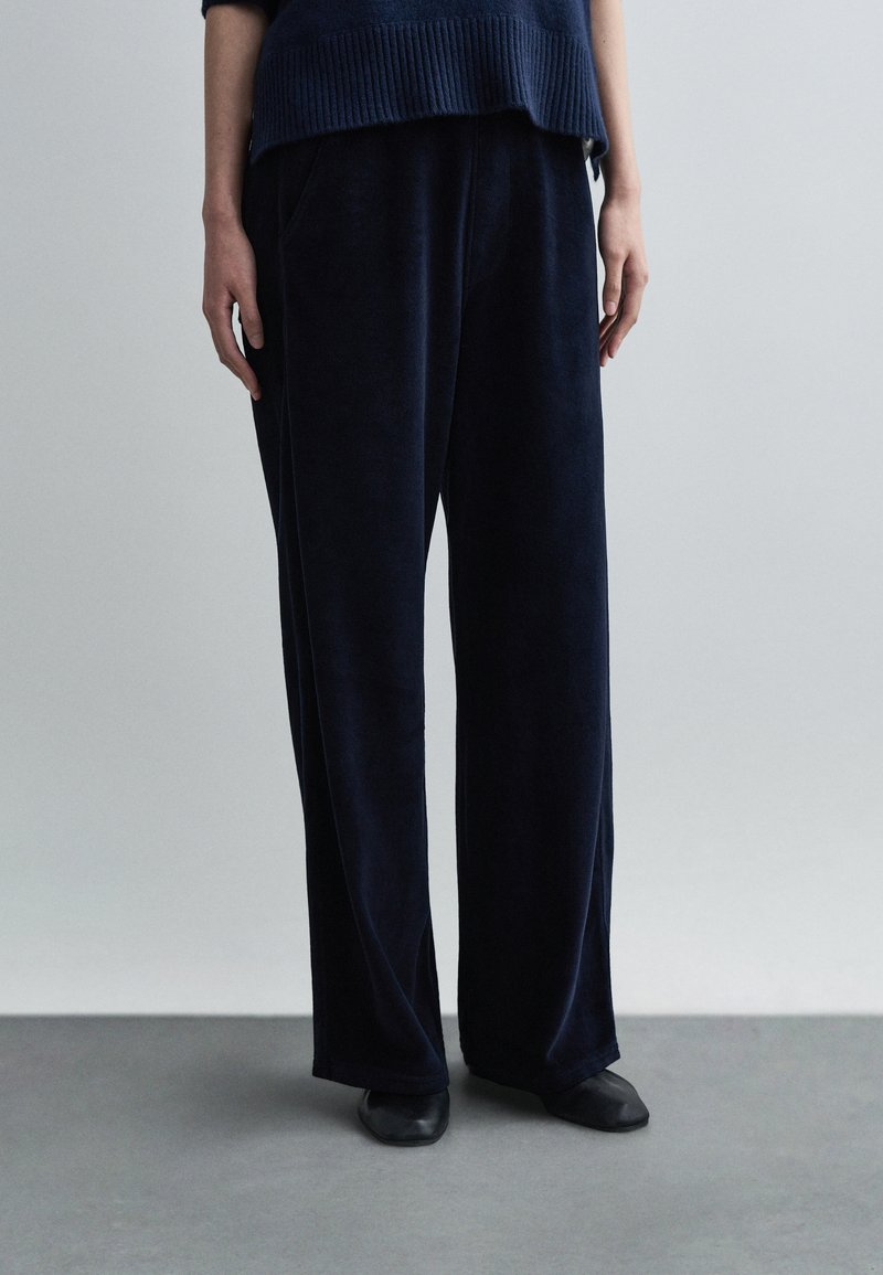 Παντελόνι με φαρδιά μπατζάκια σε ναυτικό μπλε χρ�ώμα, κατασκευασμένο από απαλό ύφασμα, με άνετη εφαρμογή, πλαϊνές τσέπες και ομαλή υφή. Συνδυασμένο με μαύρα παπούτσια.