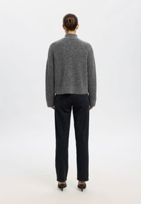 Suéter de mezcla de lana gris con un corte holgado, cuello alto y hombros caídos, combinado con jeans negros de talle alto y tacones negros.