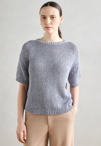 Világosszürke kötött pulóver rövid ujjal, texturált mintával, kerek nyakkal és bordázott aljjal, bézs nadrággal párosítva. Egyszerű dizájn.