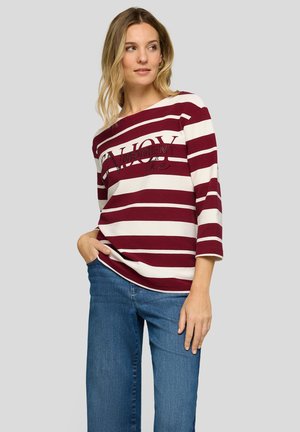 Langärmliges Shirt mit bordeauxroten und weißen Streifen, weitem Ausschnitt und Textdetail. Kombiniert mit blauen Jeans in entspannter Passform.