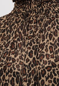 Tela de estampado de leopardo con fondo color beige, con manchas marrón oscuro. El material tiene una textura suave y detalles fruncidos en la parte superior.