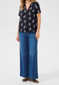 Navy floral short-sleeve blouse with a V-neck, paired with wide-leg blue denim jeans and brown shoes. Blouse features white floral pattern.