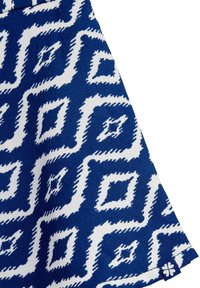 Kék és fehér geometrikus mintázatú, gyémántformákkal díszített pamutszövet. Az alsó jobb sarokban egy kis logó címke található.