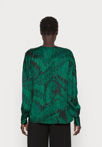 Grön och svart virvlande mönsterblus med långa ärmar, rund halsringning och knappade manschetter, tillverkad av ett mjukt och lätt tyg.