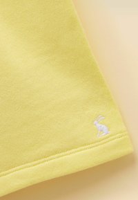 Coin de tissu jaune avec couture visible et un petit lièvre blanc brodé près de l'ourlet sur un fond clair.