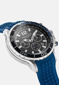 Nautica kroonverbondi kellaga, millel on sinine silikoonrihm, hõbe värvi tahvel, must ümmardus, tekstuuriga näidik ja silmapaistvad numbrimärgid.