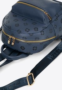 Zaino tondo blu navy con pelle testurizzata e motivi in rilievo. Dotato di zip dorate e di una tracolla regolabile con dettagli del logo.