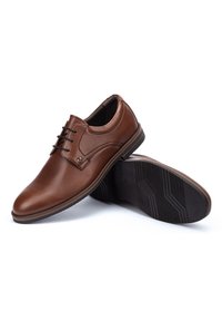 Chaussures en cuir marron avec un bout arrondi, un laçage et une semelle en caoutchouc texturée. Présentent des coutures discrètes et un talon bas.