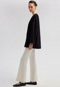Čierny oversized top s dlhými rukávmi, skombinovaný s voľnými bielymi rozšírenými nohavicami a čiernymi presúvacím obuvou. Jednoduchý dizajn s minimálnymi akcentmi.