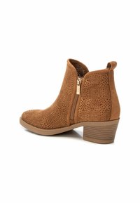 Botas de tobillo perforadas en tono marrón claro con cremallera lateral y tacón apilado. Textura de ante suave y diseño de punta redonda.