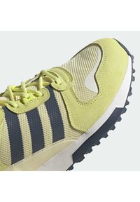 Light yellow sneaker featuring mesh and suede materials, with navy stripes, textured detailing, and a rugged black rubber sole.