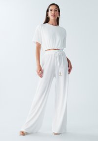 Biały krótki top i spodnie o szerokich nogawkach, wykonane z teksturowanej tkaniny, z elastycznym paskiem i sznureczkami. Wygodny i prosty design.