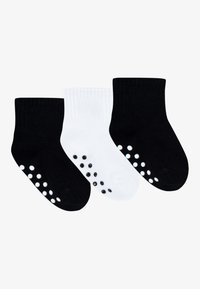Three pairs of short socks: one black, one white, and another black. Each has rubberized dots on the soles for grip. Ribbed cuffs.