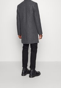 Cappotto grigio in misto lana con taglio dritto, colletto alto e cuciture a vista, abbinato a pantaloni neri attillati e stivali Chelsea neri.