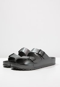 Svarta träskor gjorda av slät, hållbar plast med två justerbara spännen. Slip-on-design med en texturerad sula för bra grepp.