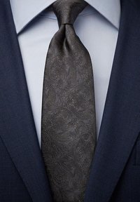Mörk paisleymönstrad slips i texturerad siden, parat med en ljusblå skjorta och marinblå kostymjacka, som visar upp intrikata detaljer.