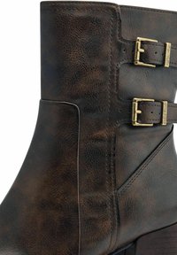 Bottine en cuir marron avec une tige incurvée, accents de double boucle et finition texturée, avec un talon robuste et des détails de couture.