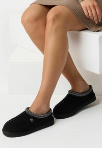 Sorte slip-on sko med en blød ruskinds tekstur, der har en kontrastsyet kant rundt om kraven og en flad gummisål.