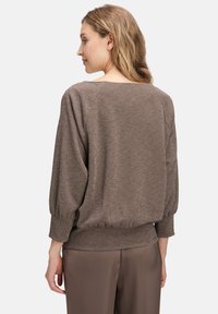 Bruine, loszittende trui met een glanzende textuur, ballonmouwen en een geribbelde zoom. Heeft een bootnel en raglan mouwnaden.