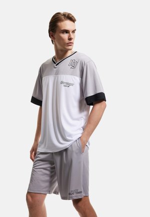 Sportoutfit voor heren met een grijs en wit shirt met korte mouwen en zwarte accenten, gecombineerd met bijpassende grijze shorts, gemaakt van lichtgewicht stof.