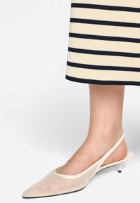 Slingback podpätky z mäkkej tkaniny v béžovej farbe s špicatou špičkou, tenkým podpätkom a textúrovaným materiálom. Navrhnuté s minimalistickými akcentmi.