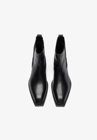 Botas de cuero negras hasta el tobillo con una punta afilada y paneles laterales elásticos. Textura suave, tacón plano y diseño minimalista.