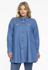 Jeanshemd, hellblau, langärmlig, mit Knopfleiste vorne, zwei Brusttaschen mit V-förmigen Akzenten, lockerer Schnitt, weicher Stoff.