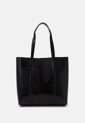 Sort tote taske med krokodillemønster, to lange håndtag og en rektangulær form mod en ensfarvet lys baggrund.