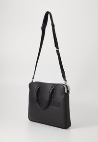 Sac à dos en cuir noir pour ordinateur portable avec deux poignées supérieures et une sangle croisée ajustable. Doté d'une surface texturée et d'accents en matériel argenté.