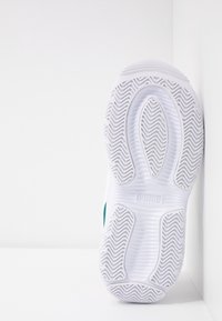 Weiße Puma-Sneakersohle mit einem strukturierten Zickzack-Griffmuster, fotografiert vor einem weißen Hintergrund in einer Ecke.