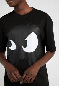 T-shirt in cotone nero con un grande design di occhio cartoon bianco in uno stile fuzzy e testurizzato. Maniche corte e vestibilità rilassata.