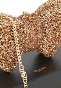Goudkleurige strikclutch bedekt met amberkleurige rhinestones en een gouden ketting, rustend op een zwarte doos met het label "Dune London."