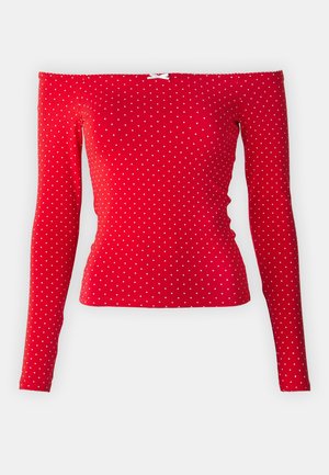 Top rojo de hombros descubiertos con mangas largas, hecho de tela acanalada, que presenta lunares blancos y un pequeño lazo blanco cerca del escote.