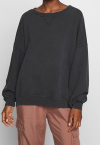 Tummanharmaa, ylivertainen collegepaita, jossa roikkuvat olkapäät, resorit hihansuissa ja helmassa. Pehmeä rakenne ja rento istuvuus. Yhdistetty vaaleanpunaisten cargohousujen kanssa.