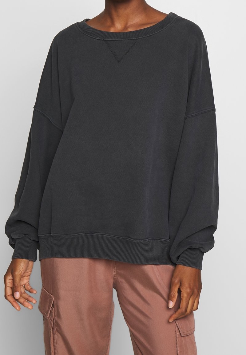 Tummanharmaa, ylivertainen collegepaita, jossa roikkuvat olkapäät, resorit hihansuissa ja helmassa. Pehmeä rakenne ja rento istuvuus. Yhdistetty vaaleanpunaisten cargohousujen kanssa.