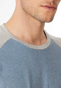 T-shirt a righe grigie e blu con maniche raglan corte. Presenta un colletto girocollo e una texture del tessuto liscia.