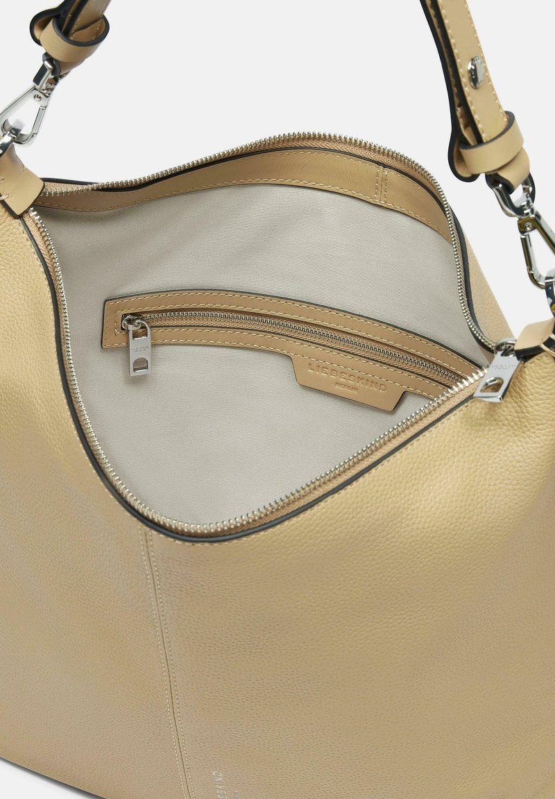 Hellbraune Lederhandtasche mit strukturiertem Finish, einem Reißverschluss oben und einem mit Stoff ausgekleideten Innenraum, der eine Reißverschlusstasche bietet.