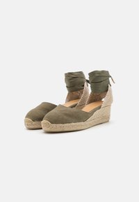 Groene canvas wig espadrilles hebben een geweven jute hak, enkelbandjes met strikdetail en een gladde textielen bovenkant.